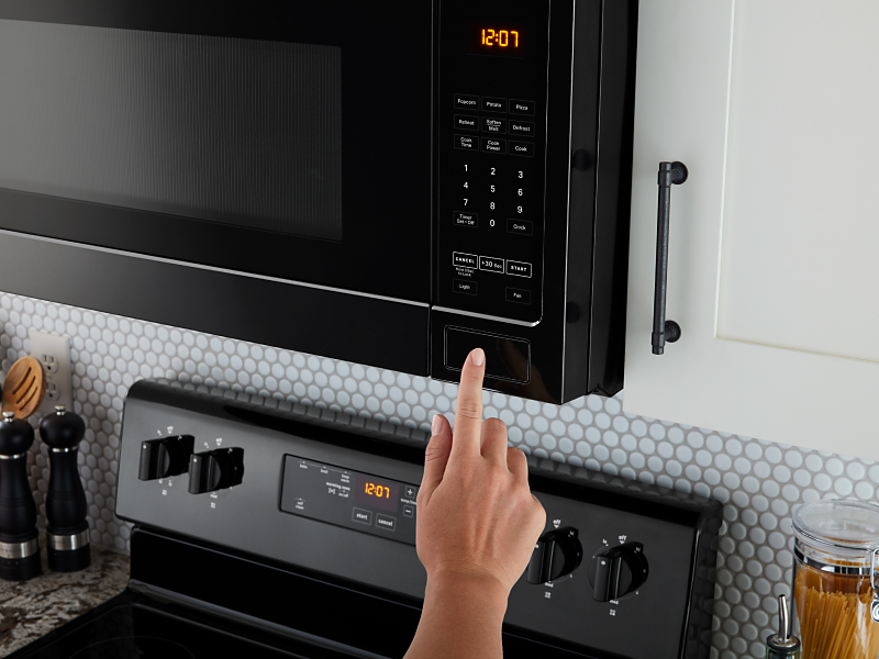 A person using a black over-the-range microwave