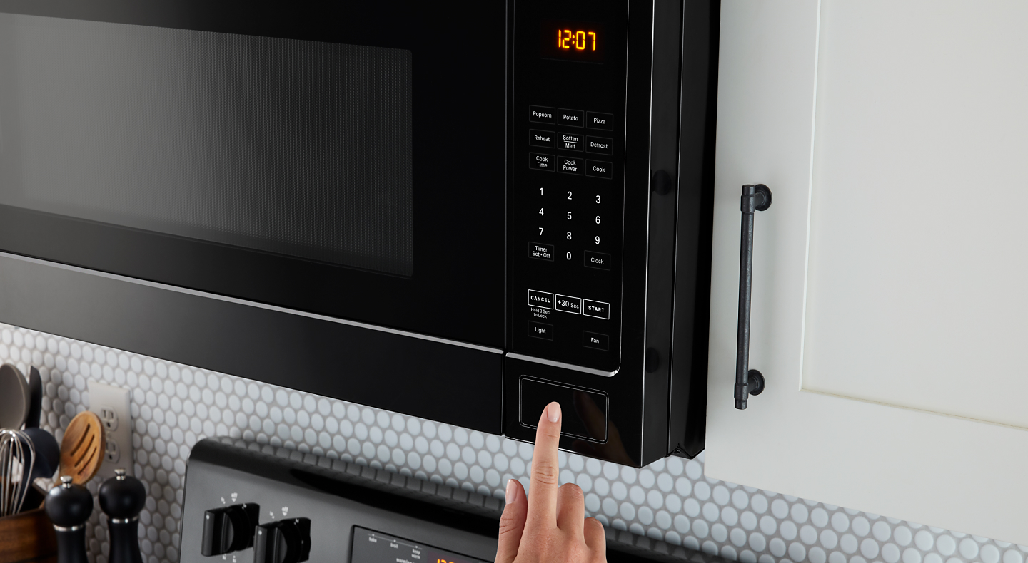 A person using a black over-the-range microwave A person using a black over-the-range microwave