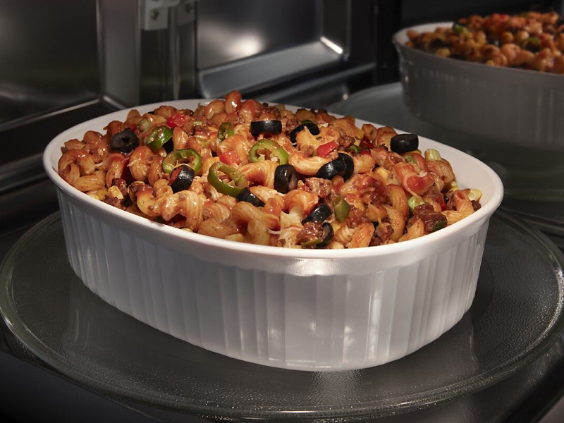 A cavatappi meal in a casserole dish heating in the microwave