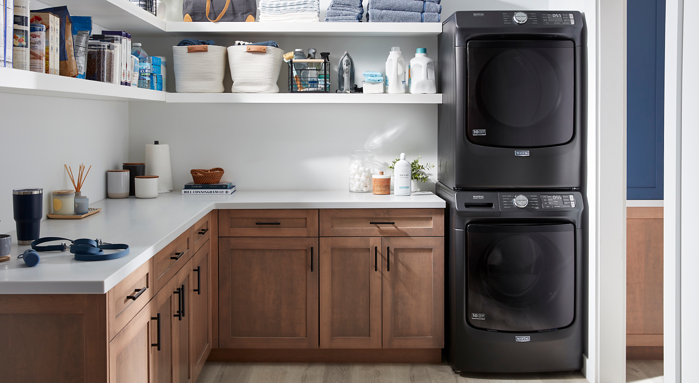 Black Maytag® front load washer and dryer pair stacked next to shelving and cabinetry