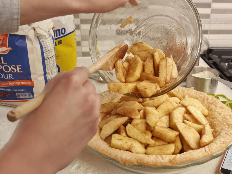 Hand preparing a pie with apple slices