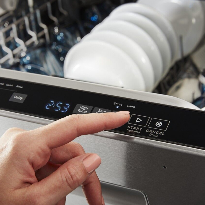 Hand touching a button on a top control dishwasher control panel