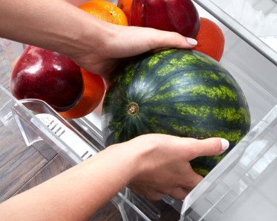 Person placing watermelon in a refrigerator