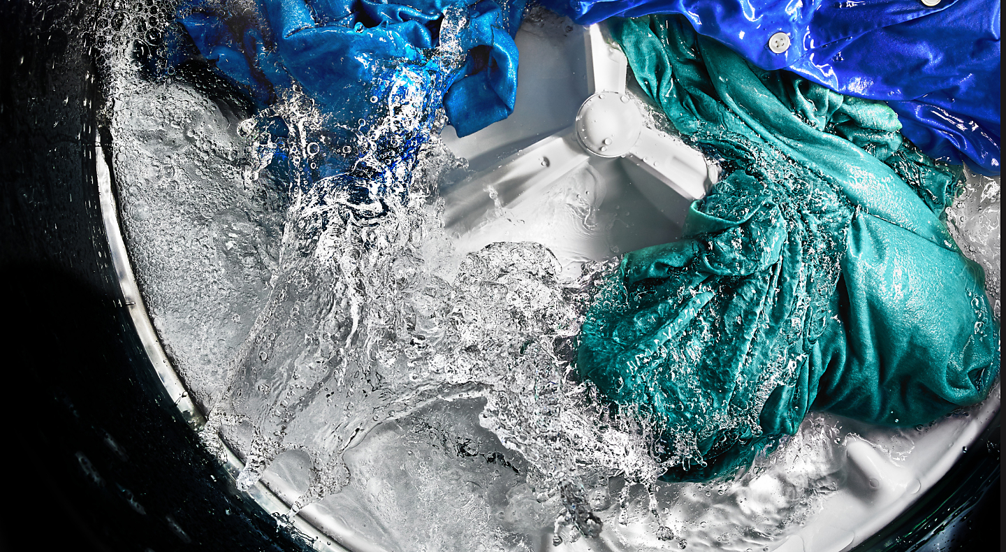 Colored clothing items spinning in water around agitator inside washing machine