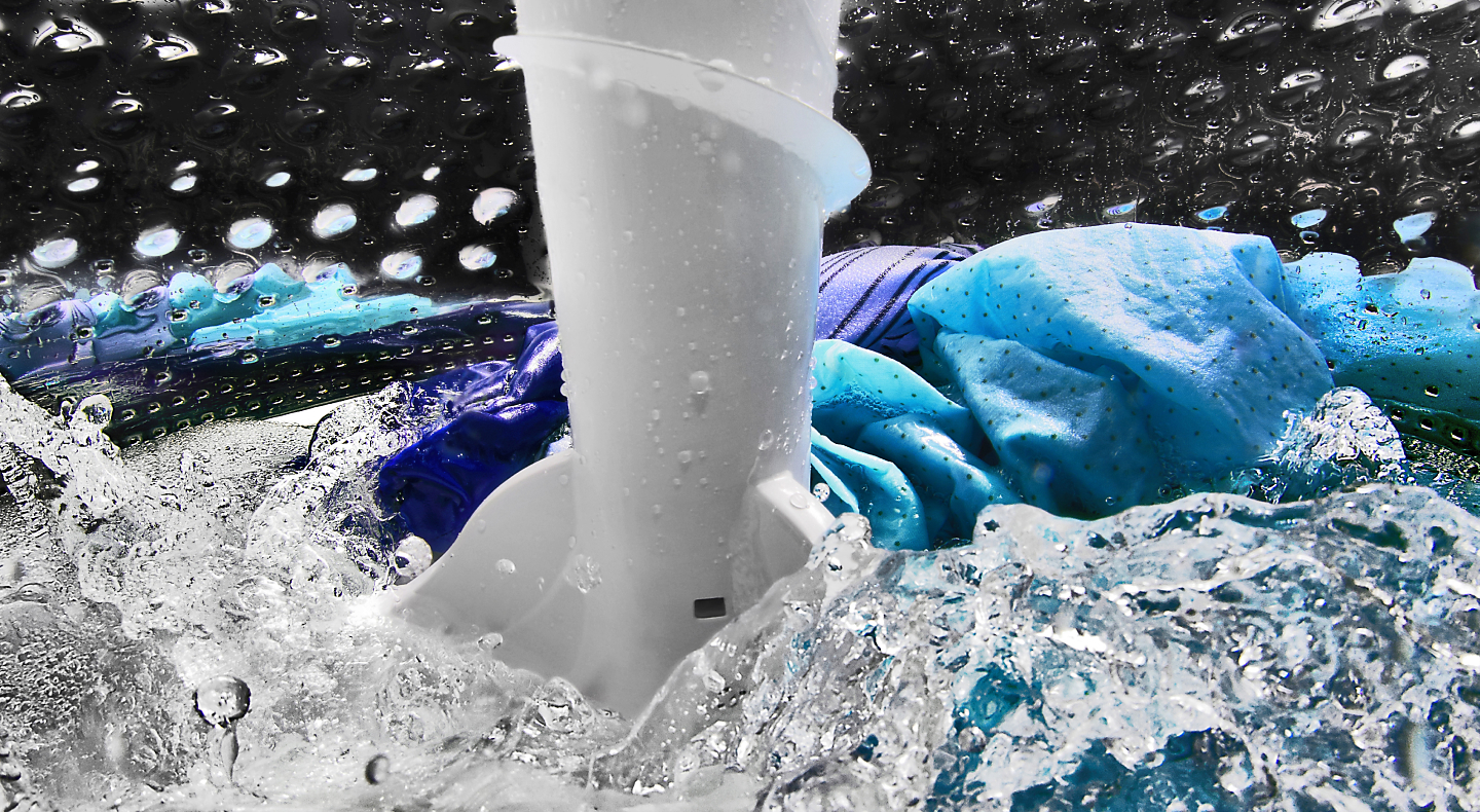 Blue and purple clothing items spinning in water in washing machine drum Blue and purple clothing items spinning in water in washing machine drum