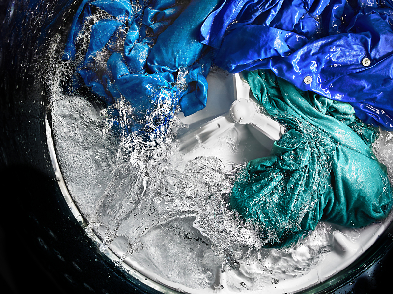 Colored clothing items spinning in water around agitator inside washing machine