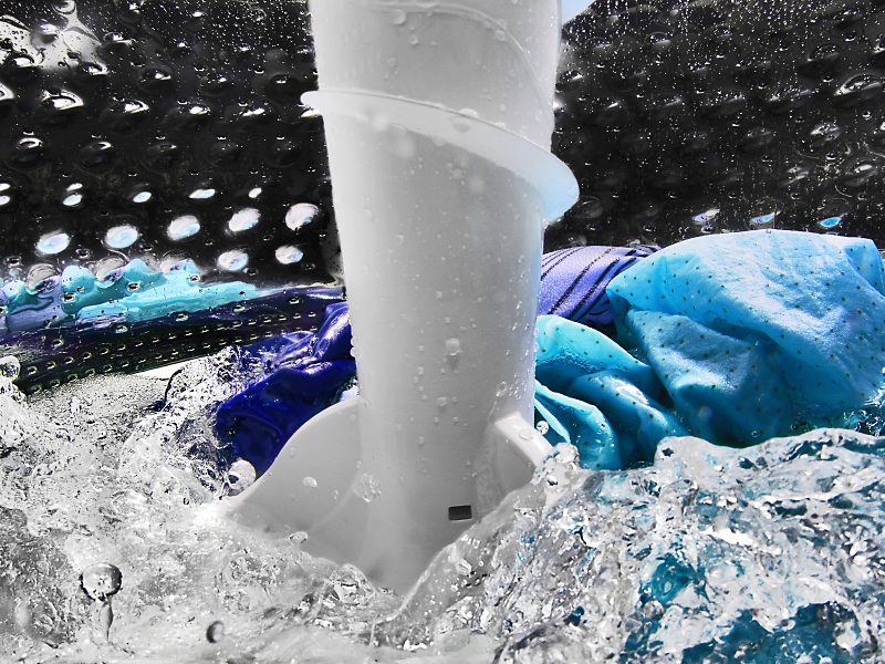 Blue and purple clothing items spinning in water in washing machine drum Blue and purple clothing items spinning in water in washing machine drum