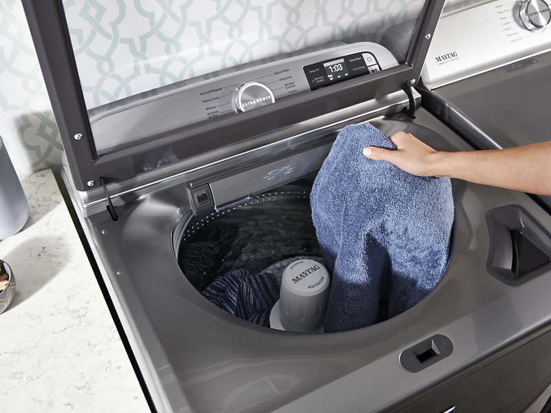 User adding towels to top load washing machine