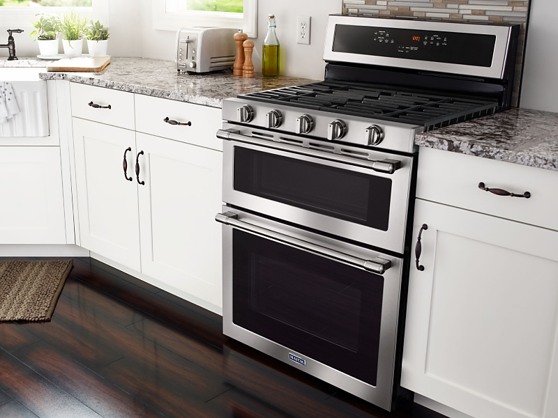 Stainless steel Maytag® gas range in kitchen between countertops and white cupboards