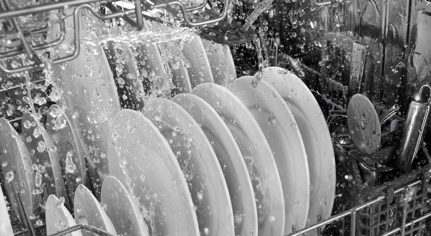 A closeup of the lower rack of the interior of a Maytag® dishwasher during a rinse cycle.