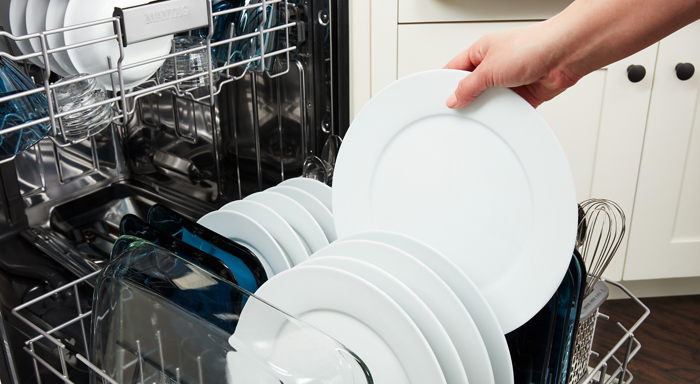  A person loading dishes into a Maytag® dishwasher.