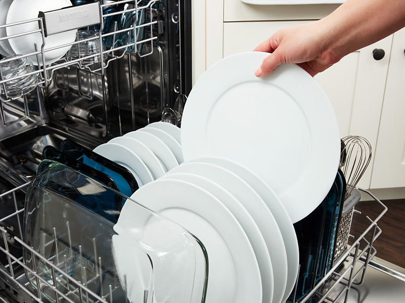  A person loading dishes into a Maytag® dishwasher.