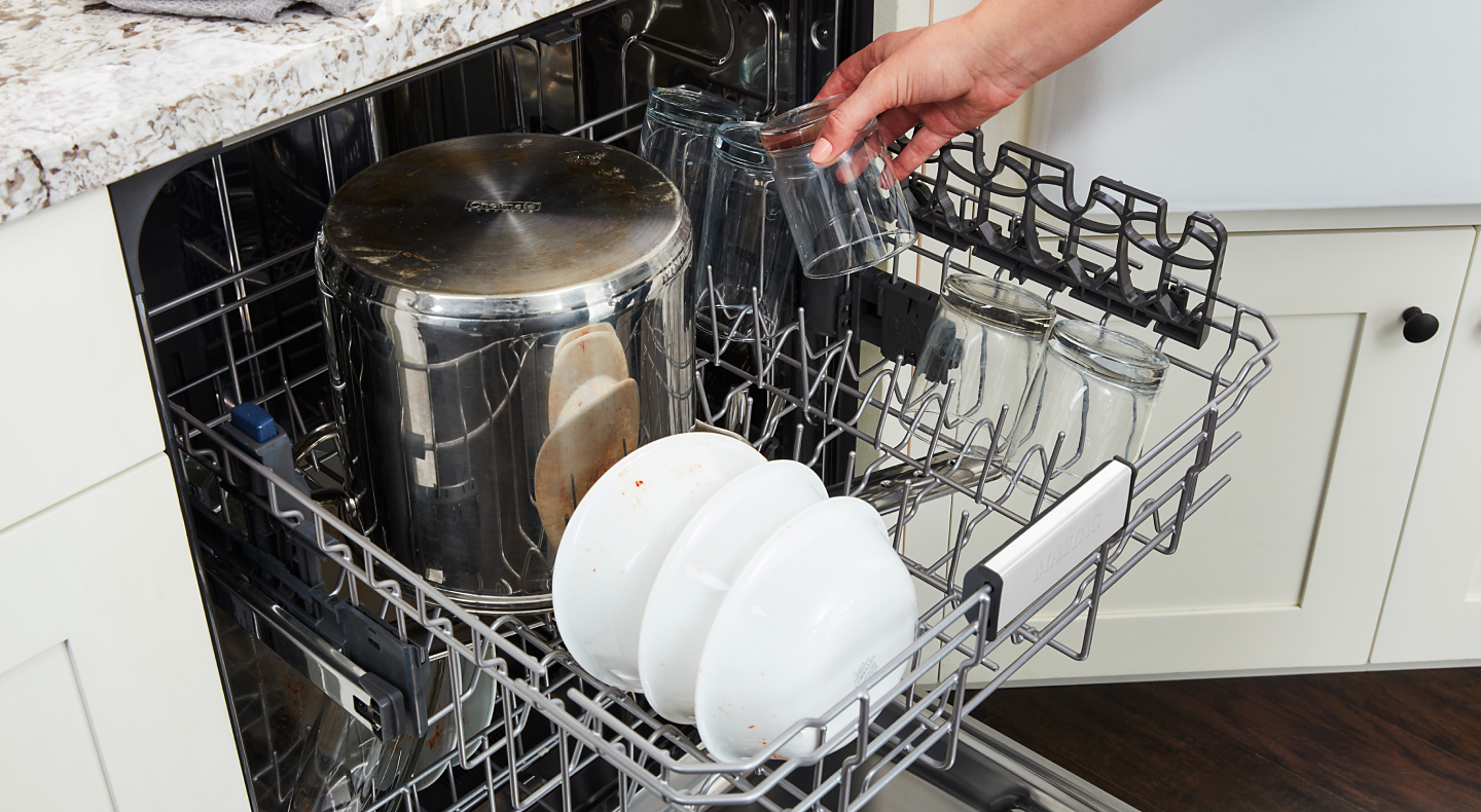 A person loading dishes into a Maytag® dishwasher.