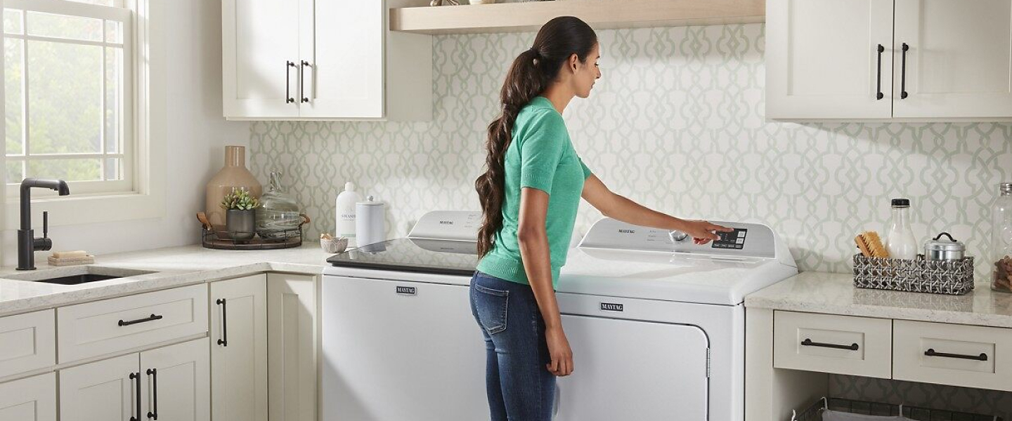 Person selecting option on a dryer in a white laundry room