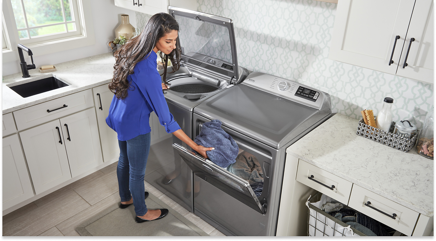 Person transferring wet clothes from a top-load washer to the dryer