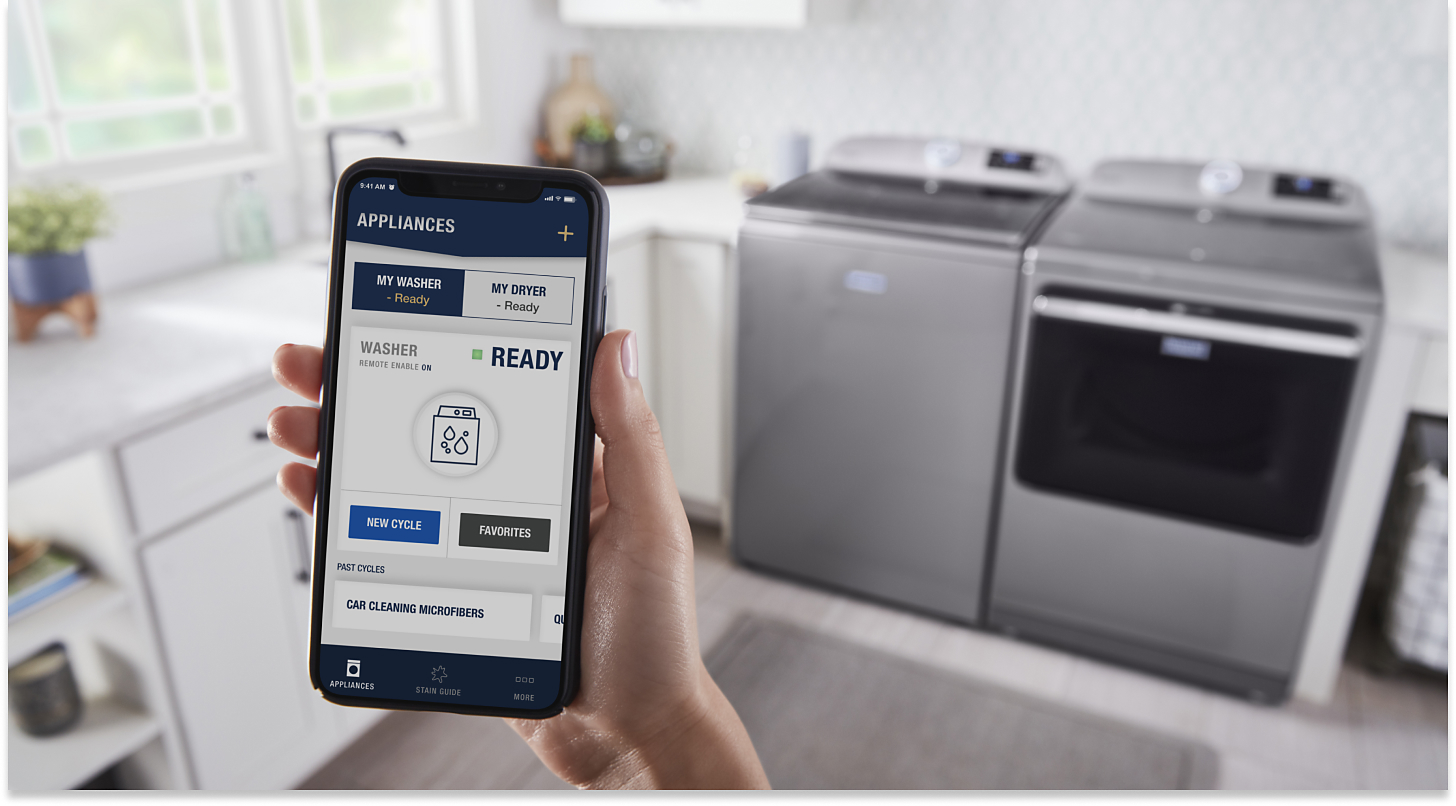 Person using the Maytag™ App standing in front of a gray top-load laundry pair