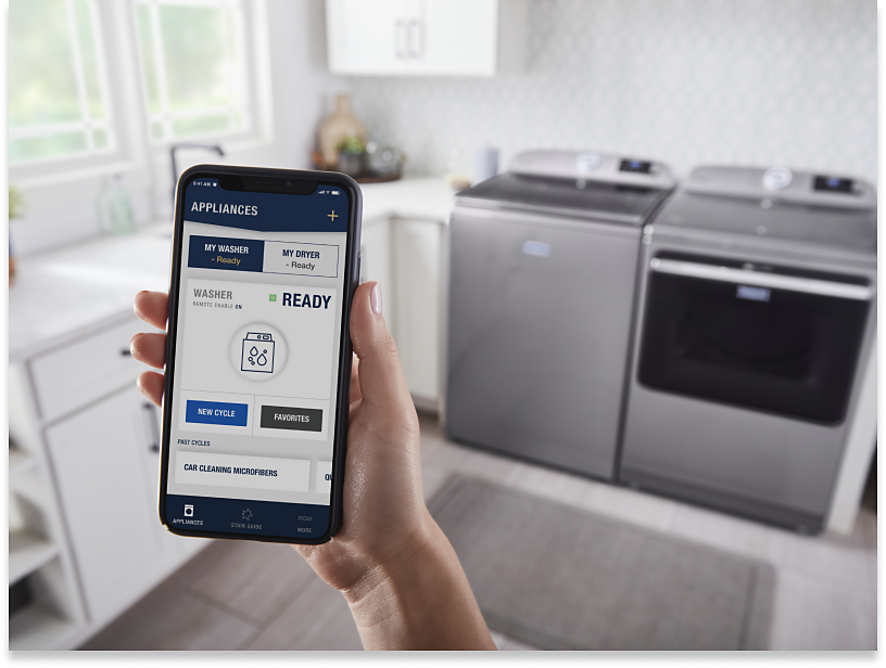 Person using the Maytag™ App standing in front of a gray top-load laundry pair