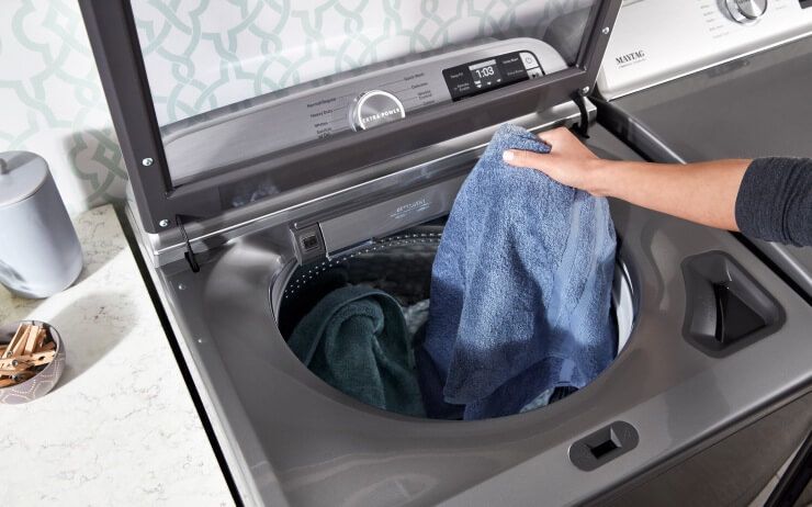 A Maytag® top load washer filled with blue clothes.
