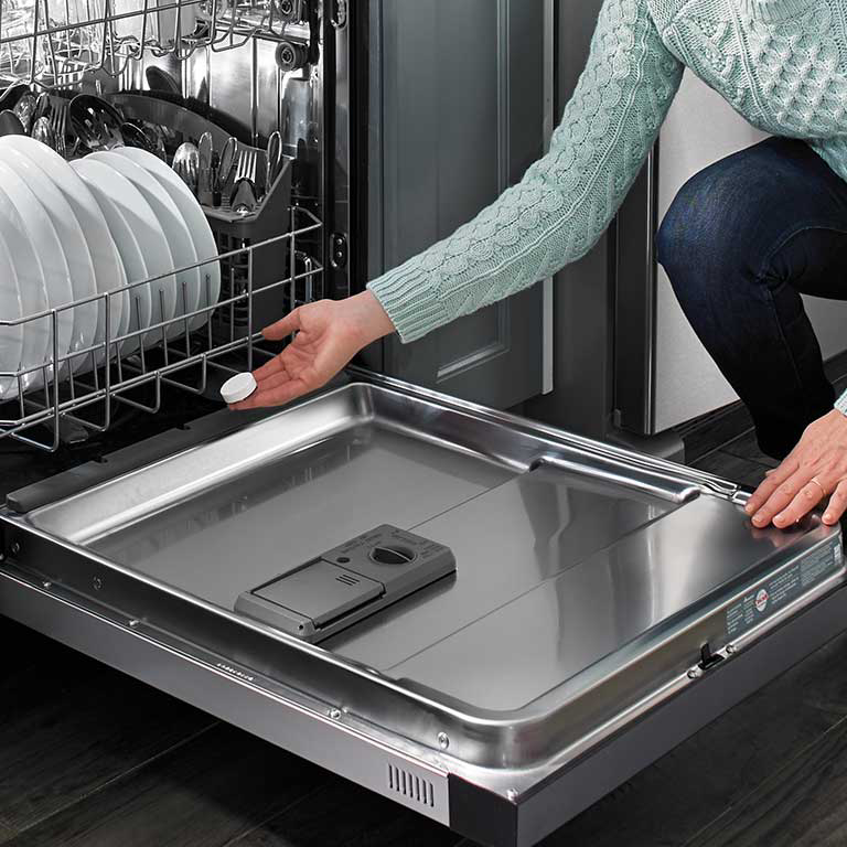 A woman placing an affresh® tablet into a dishwasher