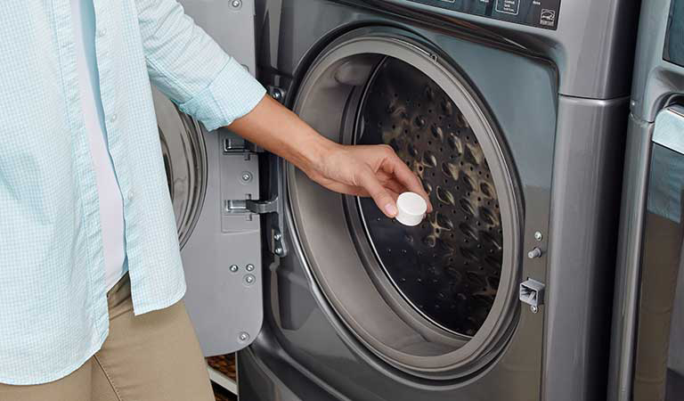 A woman placing an affresh® tablet into a washing machine