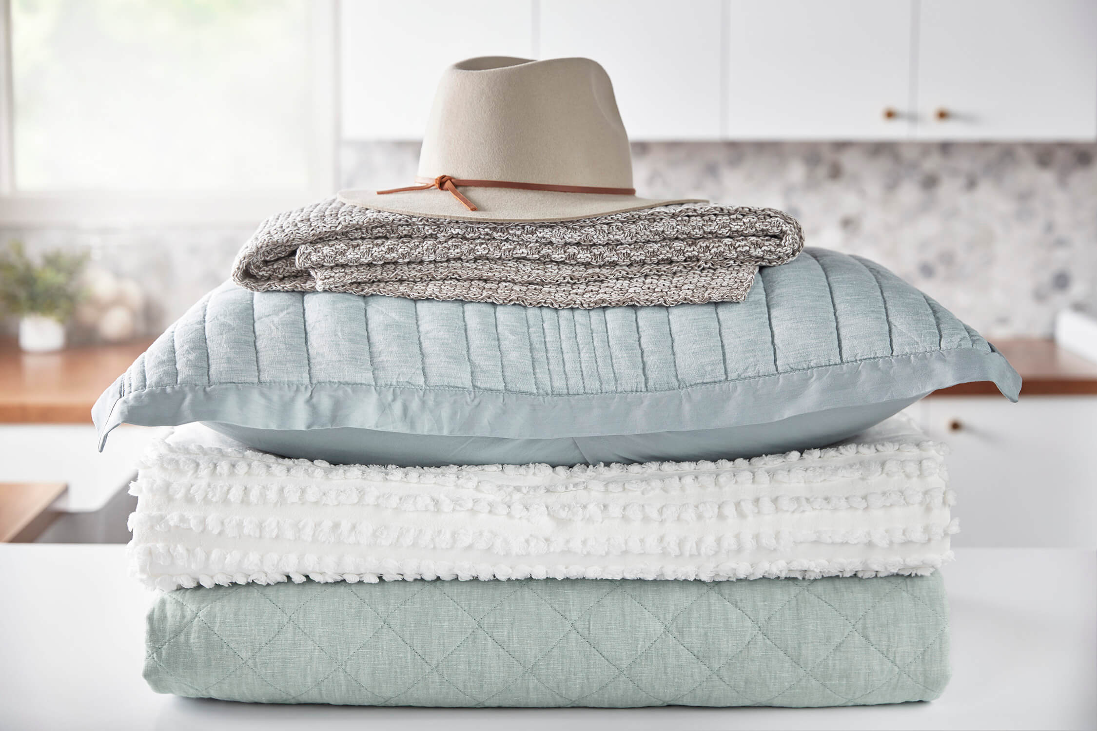 A cream colored sun hat on a stack of freshly cleaned blue linens.