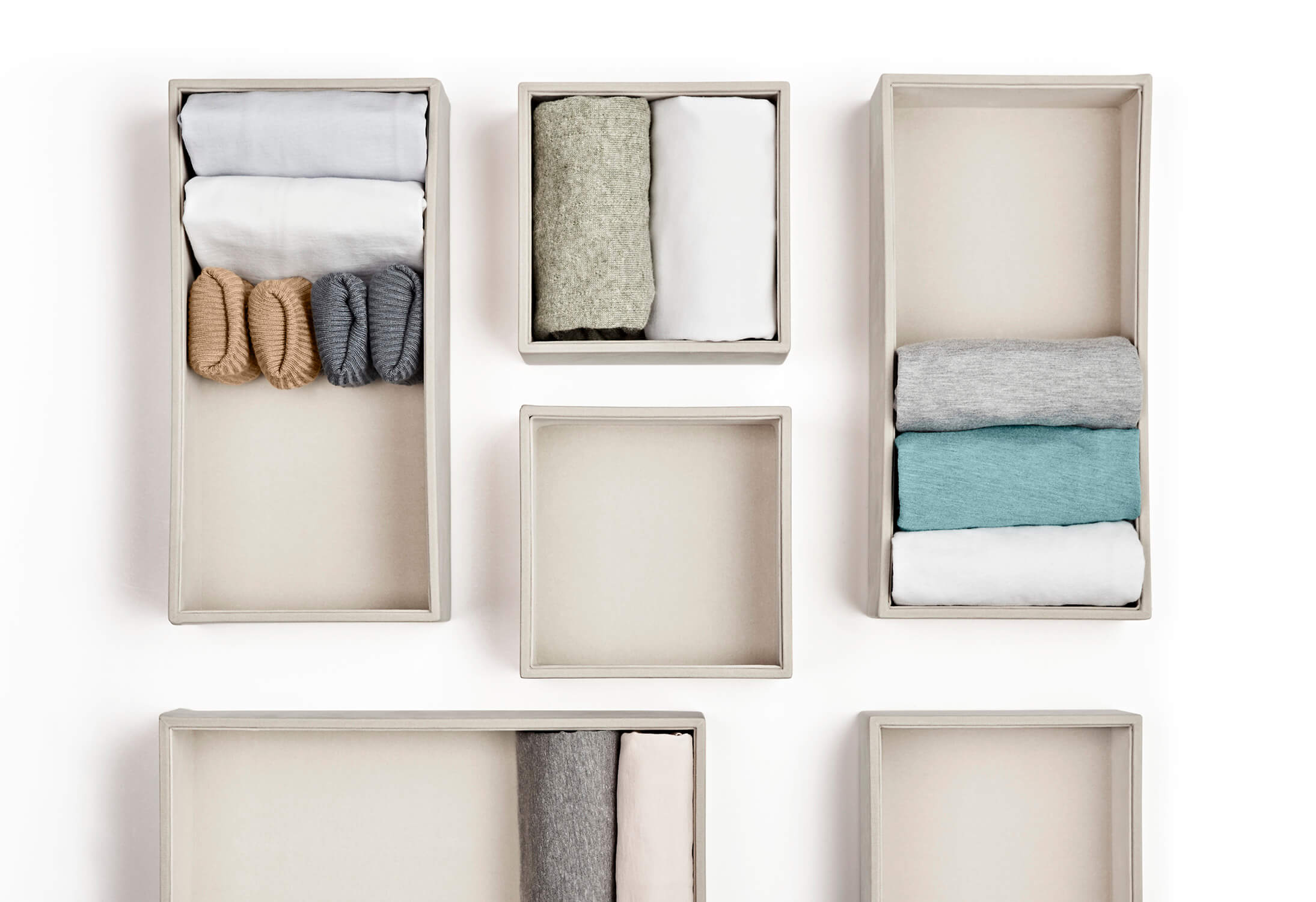 Neatly organized laundry in linen coloured organizers spaced out on a white background