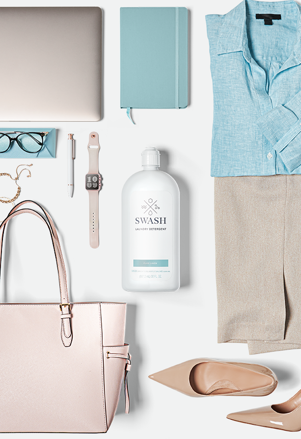 A bottle of Swash Pure Linen Laundry Detergent lies on a white surface along with clothes and assorted accessories.