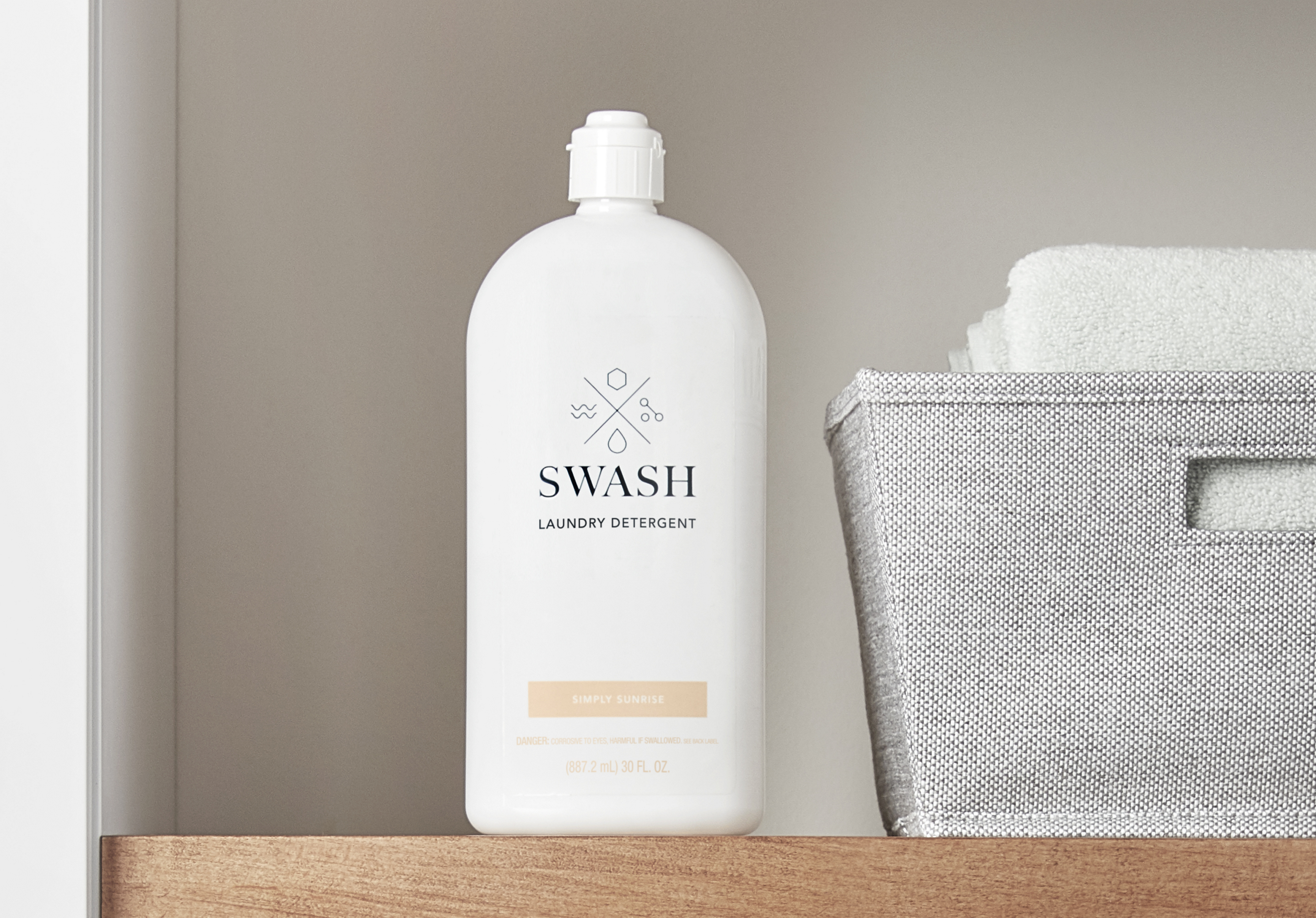Swash Simply Sunrise Laundry Detergent on a wooden shelf in a laundry room next to towels and other laundry supplies