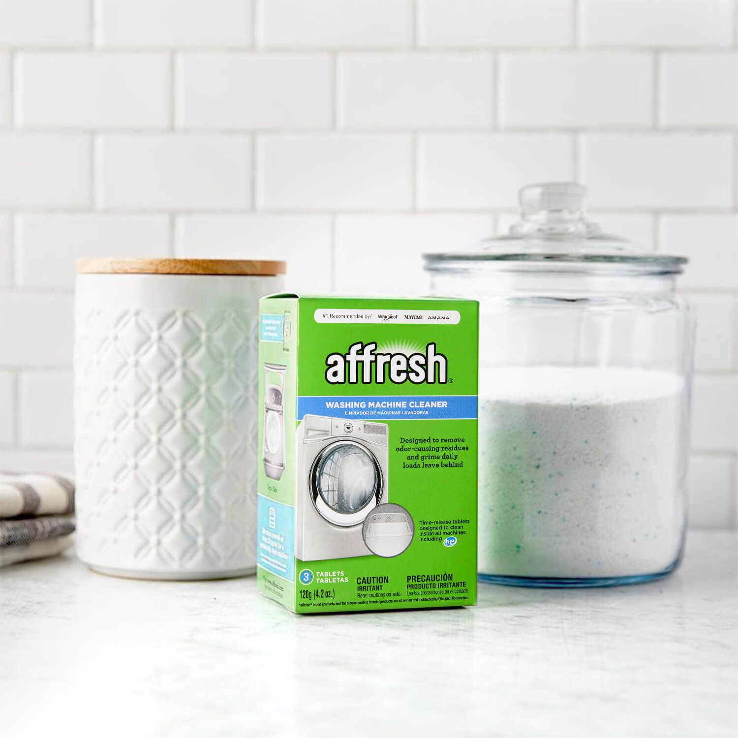 a green box of Affresh Washing Machine Cleaner tablets sitting on a white marble countertop in a laundry room