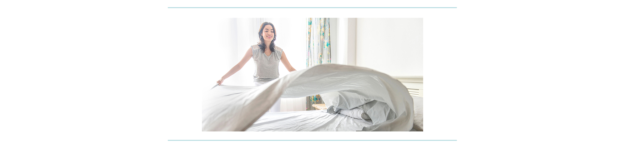 A woman puts a clean sheet on a bed.