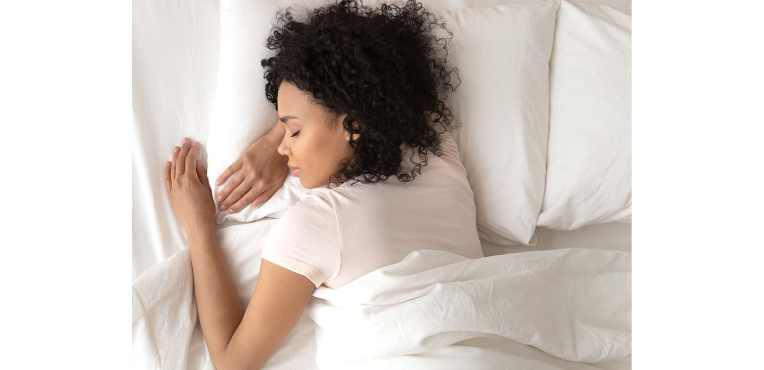 A woman sleeps on clean, white sheets with her head on a fresh pillow.