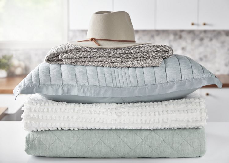 A stack of blankets and pillows with a hat on top sits on a laundry room counter.