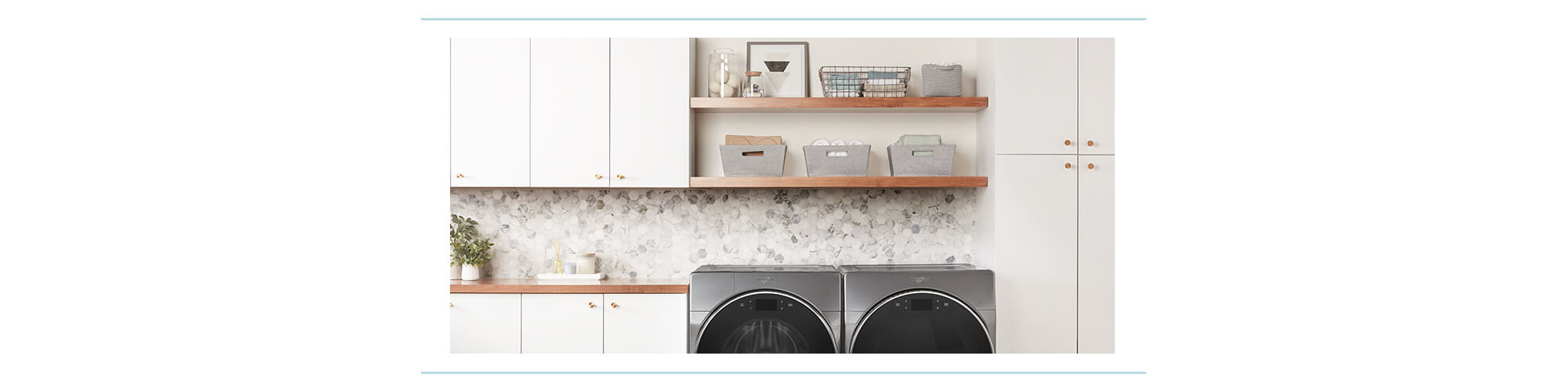A neatly organized laundry room with open shelves, white cabinets, and Whirlpool front loading washer and dryer