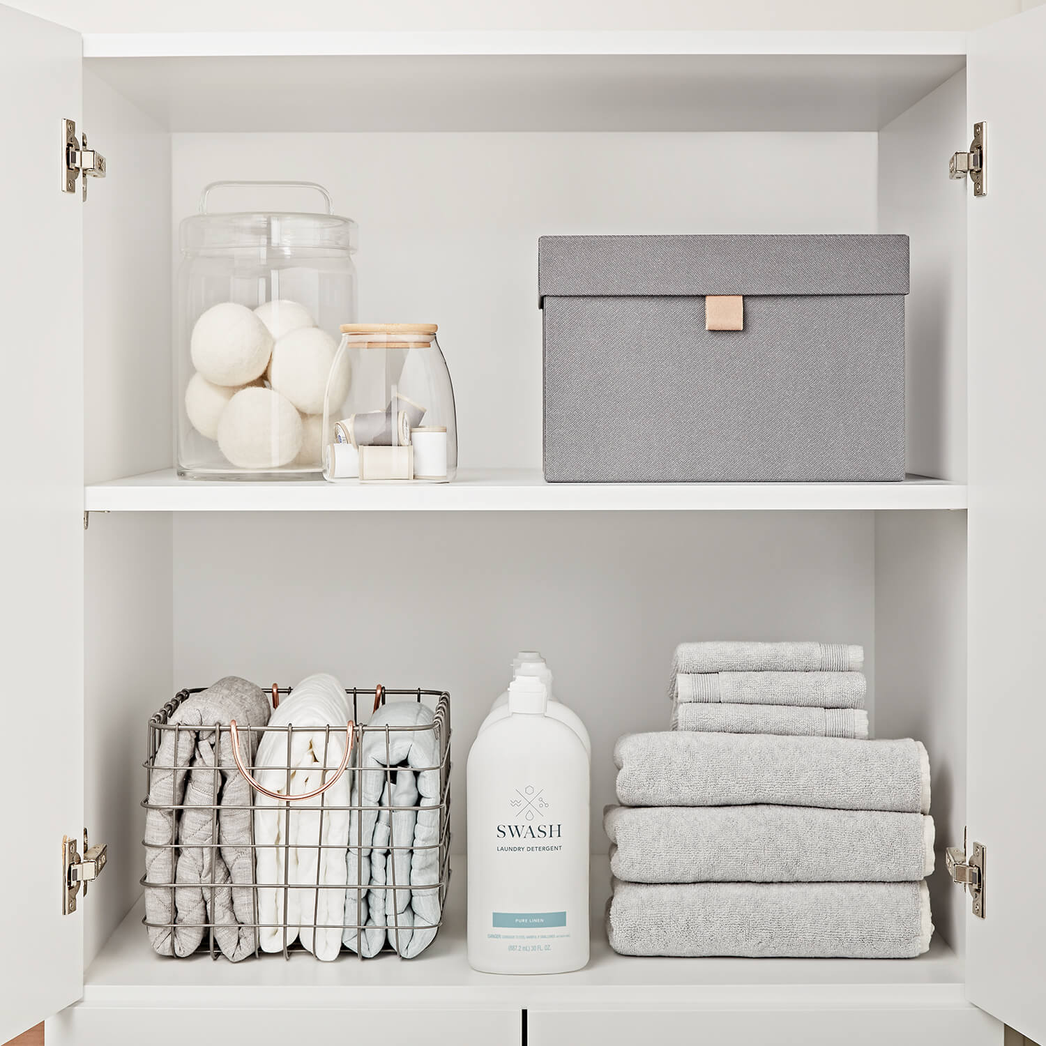 A neatly organized cabinet inside of a laundry room with fresh linens and Swash laundry detergent.