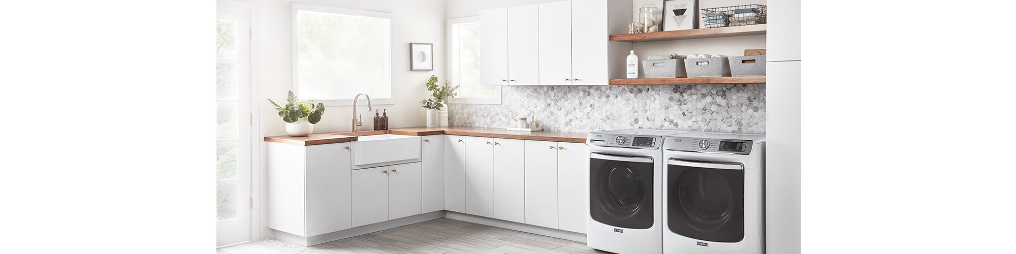 A large laundry room with white cabinets, farmhouse sink, and open shelving with neutral organizational baskets