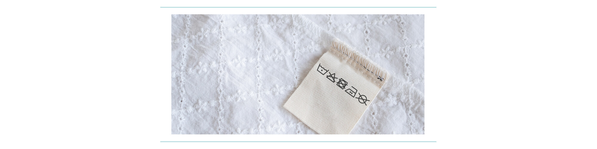 A laundry care tag with symbols on it sewn into a white eyelet piece of fabric