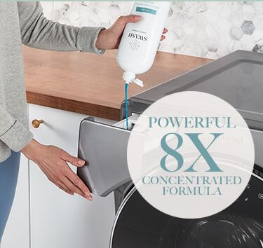 A woman in a gray sweater dispensing Swash laundry detergent into a Whirlpool washing machine dispenser drawer.