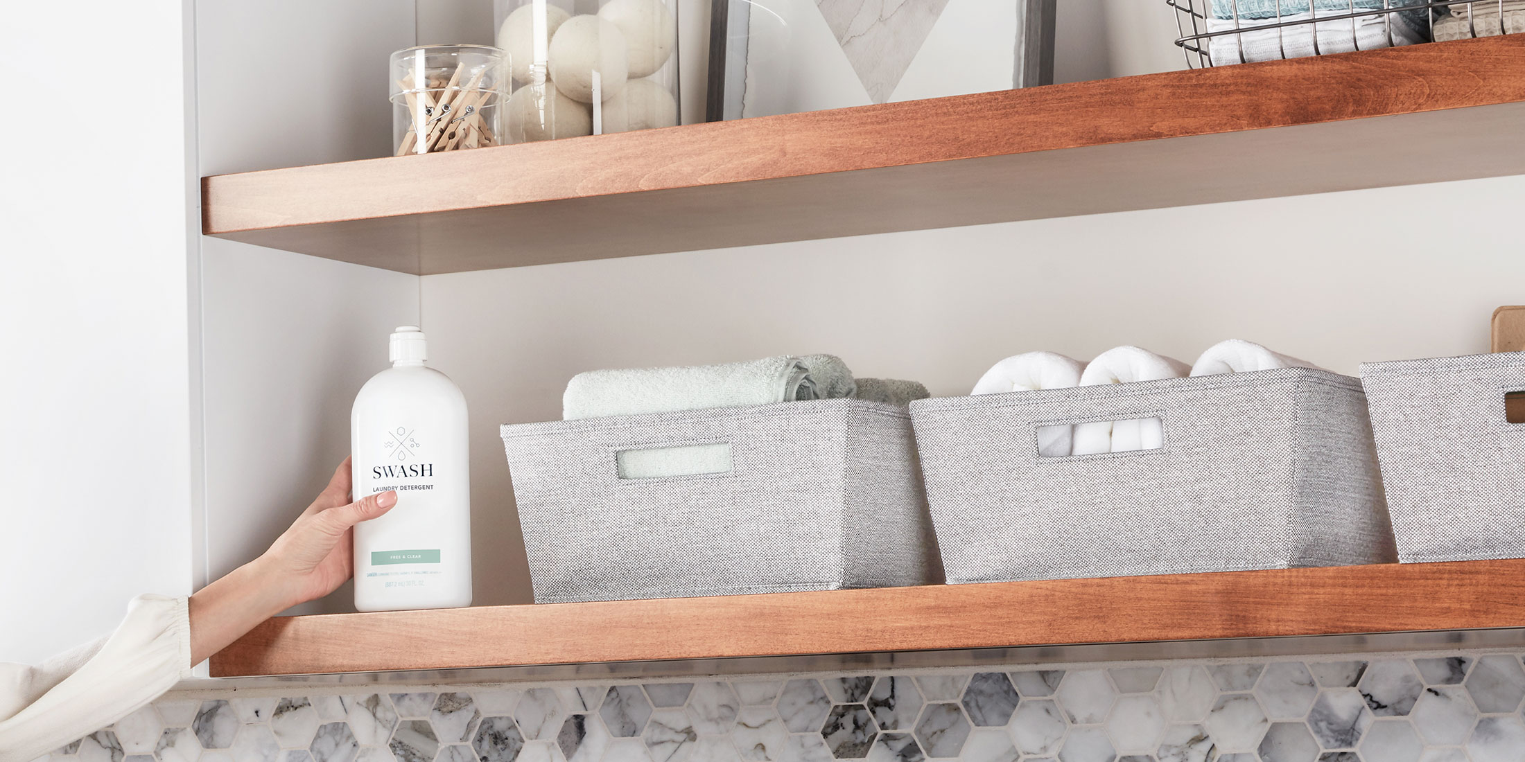 A hand placing the sleek Swash Pure Linen laundry detergent back on a wooden shelf