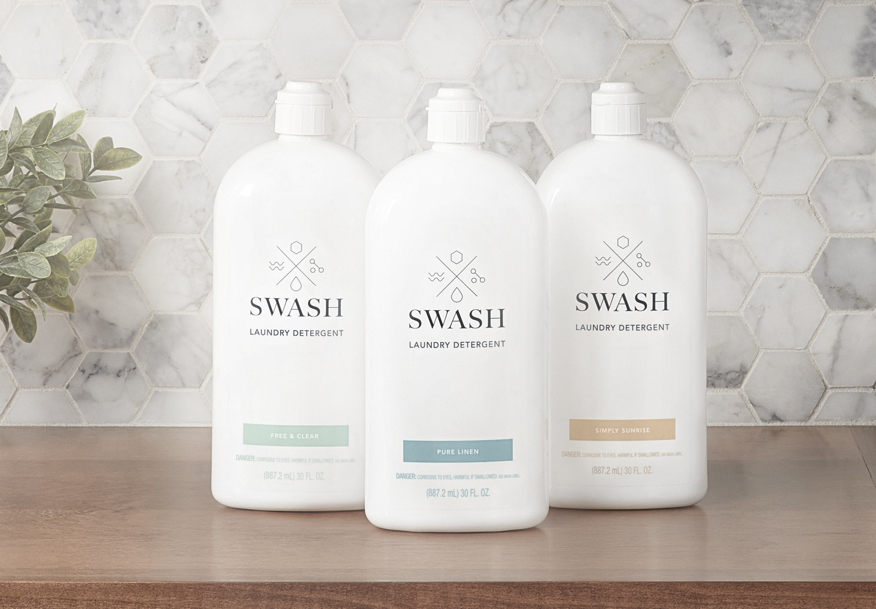 Swash Pure Linen, Free and Clear, and Simply Sunrise Laundry Detergent in sleek white bottles on a wooden surface