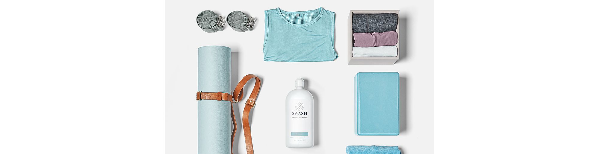 Sets of folded workout clothes and workout gear surround a bottle of Swash laundry detergent.