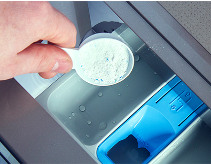 Powder detergent is poured into a washing machine dispenser.