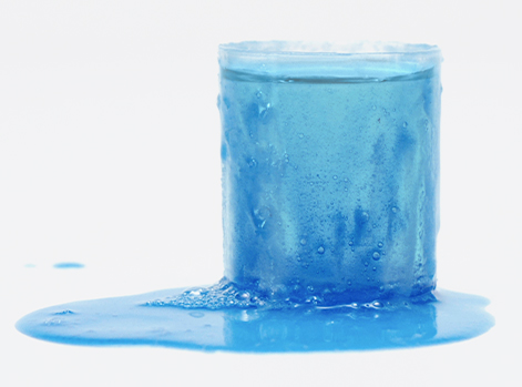 An overflowing cup of blue liquid laundry detergent.