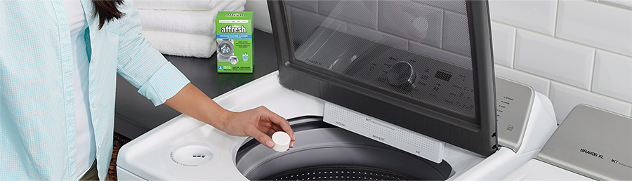 A person dropping an affresh tablet into a top loading washing machine.