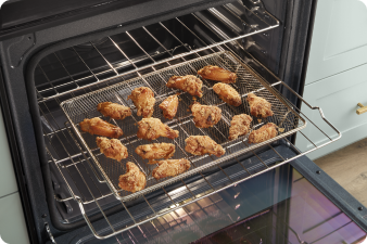 An opened Whirlpool Oven with the middle rack pulled out. On the rack is an air fry basket filled with chicken wings