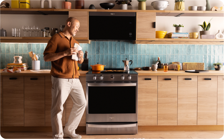 A person walking through a modern kitchen with light wood cabinets and Whirlpool brand appliances