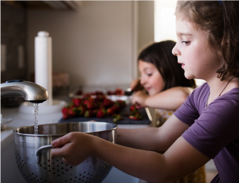Two children rinsing fruit in a sink