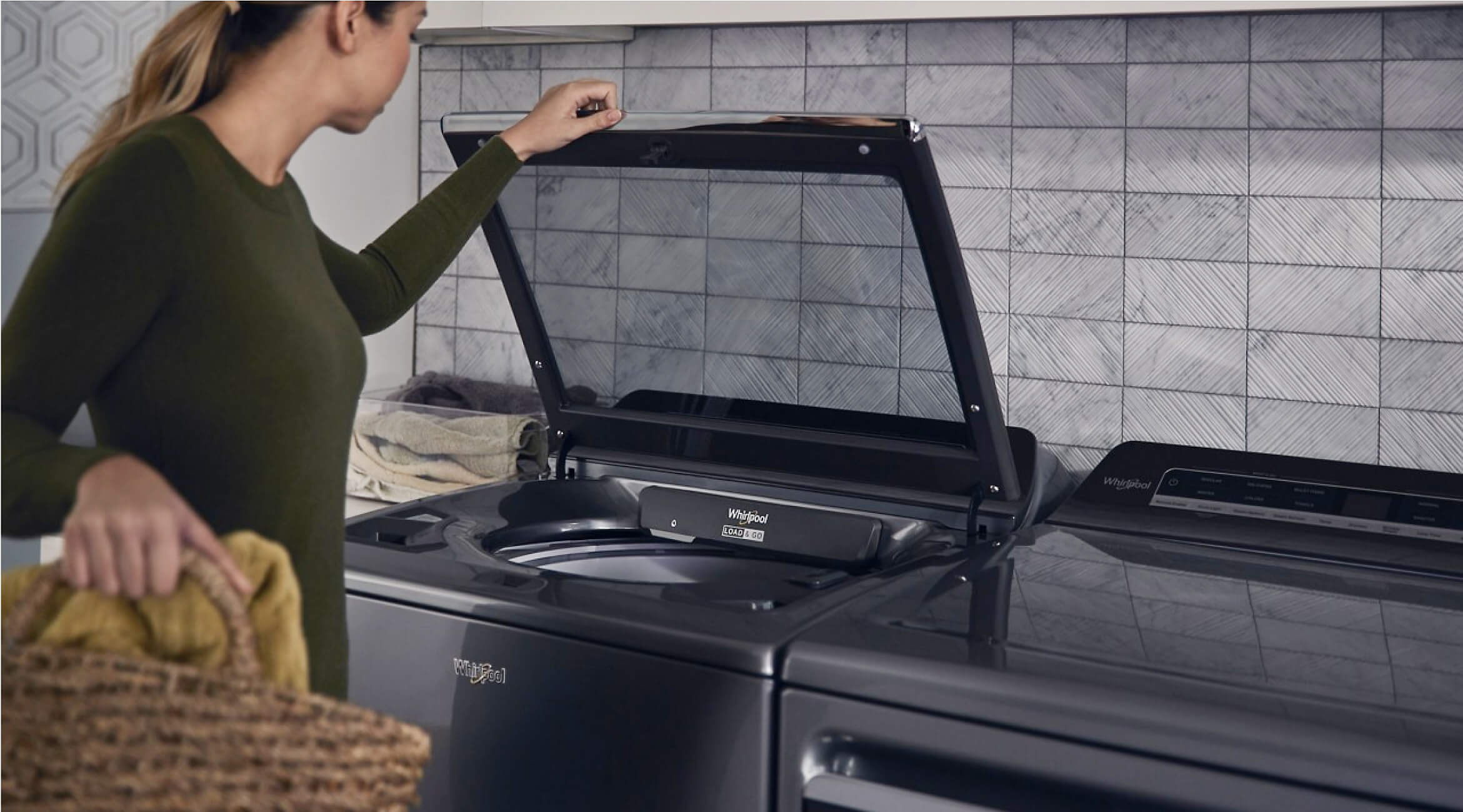 Woman holding a laundry basket and opening a Whirlpool® Top Load Washer