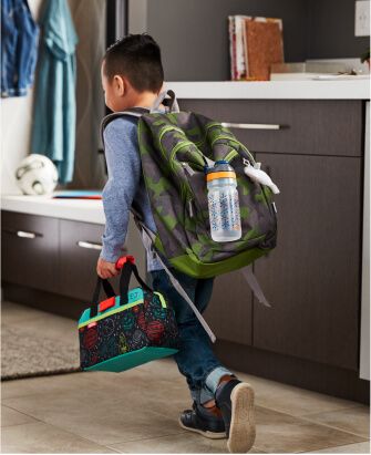 Jeune garçon avec sac à dos et boîte à dîner s’apprêtant à partir, avec une bouteille d'eau pleine suspendue à son sac