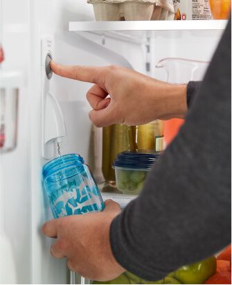 The inside of a fully stocked refrigerator, someone is filling up a reusable water bottle from the internal refrigerator water filter