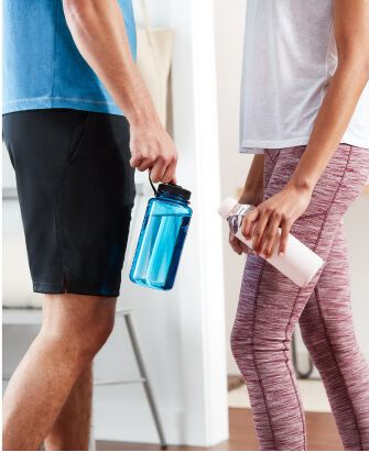 Two people in workout clothes hold their reusable water bottles